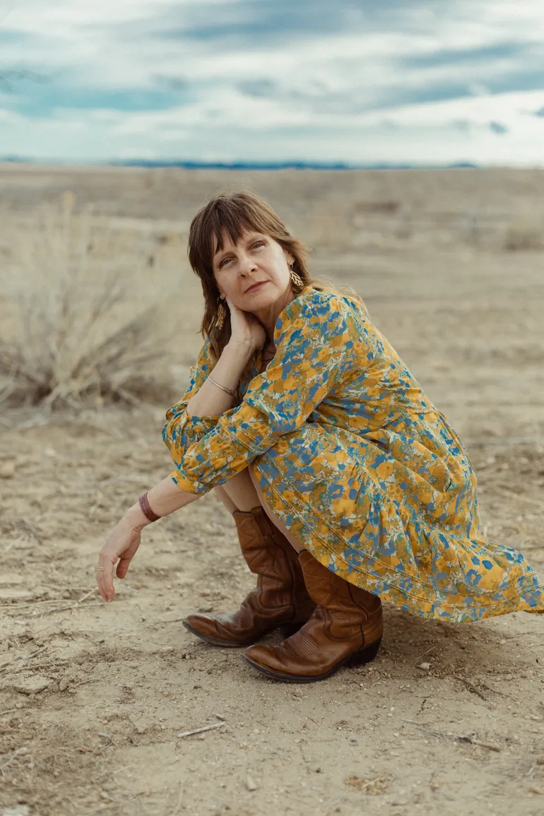 A woman wearing a dress crouched against an arid landscape.